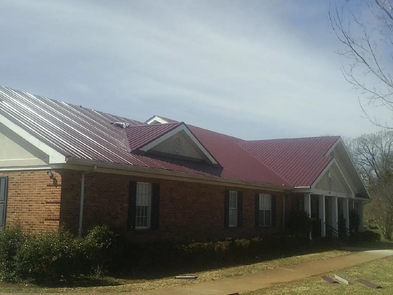 Red metal roof with gabled entries on a long brick building, from a Hail Damage Roof Repair job in Jackson Center