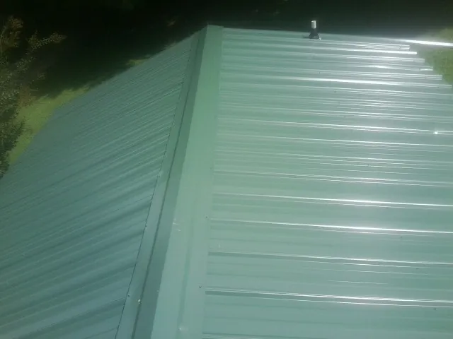 New green metal panels meeting at the ridge of a roof — Flat Roof Repair work by our crew in Jackson Center