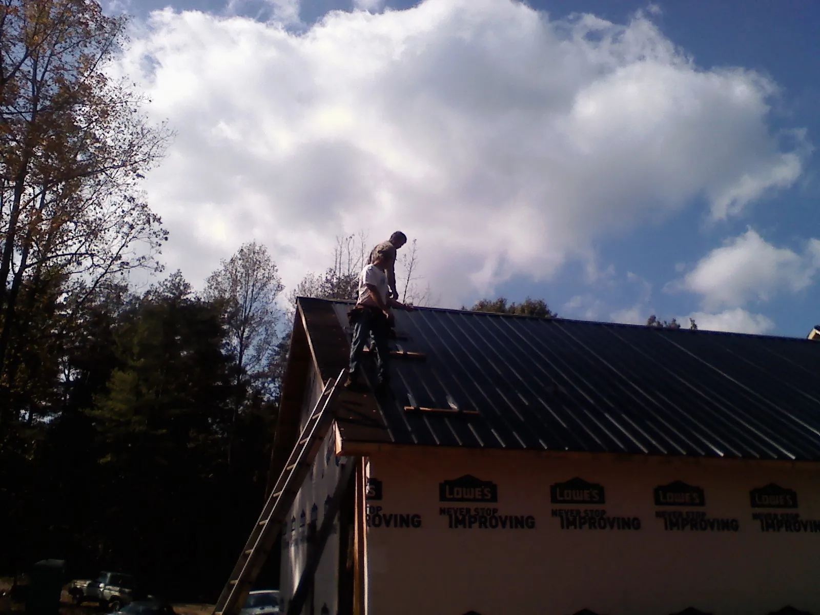 Roofer fastening dark metal panels high against a cloudy sky, from a Roof Inspection job in Jackson Center